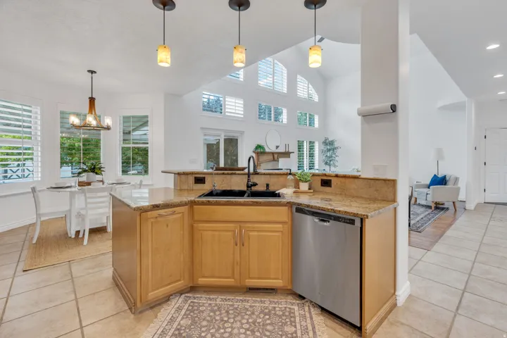 Kitchen featuring light wood cabinetry, granite countertops, a built-in stainless steel dishwasher, and a black sink with a gooseneck faucet