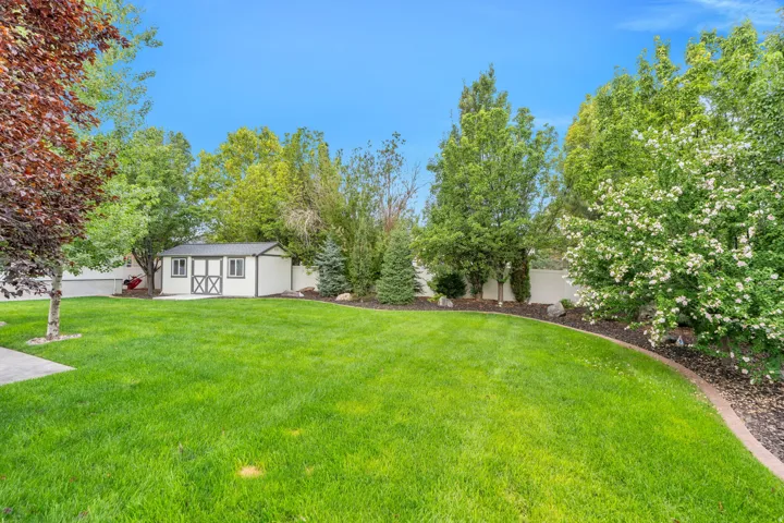 Expansive lawn area, detached storage shed with double cross-buck doors, mature trees, and landscaped borders