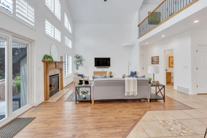 Spacious living area featuring a vaulted ceiling, wood-finish flooring, and a fireplace with a wood mantle