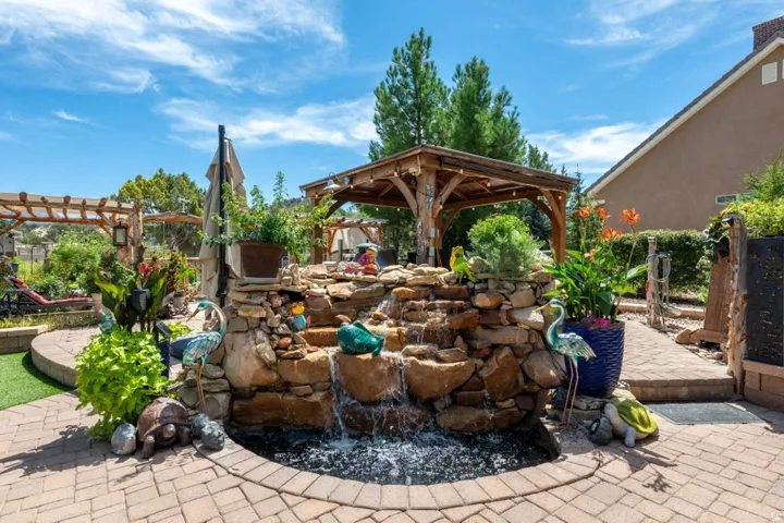 Expansive backyard featuring a multi-tiered rock waterfall, a wooden pergola, a separate wooden gazebo, a paver patio, and lush landscaping