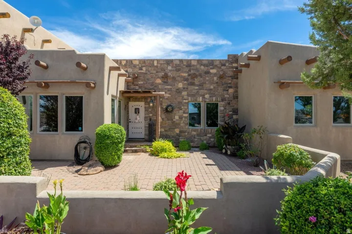 Stucco exterior featuring exposed wooden vigas, a stone facade, and a paver courtyard