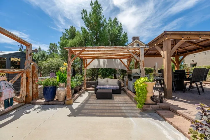 Outdoor living space featuring a wood pergola with fabric shade, a separate wood gazebo with string lighting, and a paved patio area