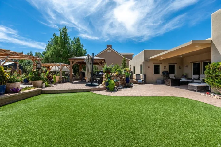 Expansive backyard featuring a manicured lawn, paver patio, covered patio, and multiple wooden pergolas