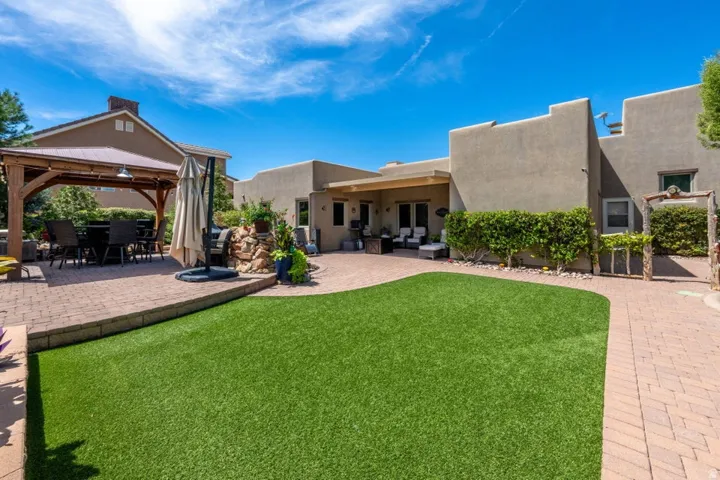 Expansive backyard featuring artificial turf, a brick paver patio, and a covered gazebo with a metal roof