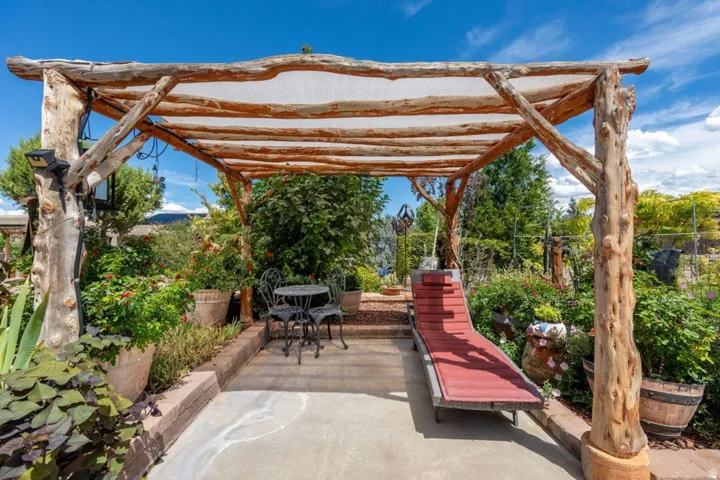 Concrete patio with a rustic wood pergola featuring a fabric cover, surrounded by raised planters with established greenery