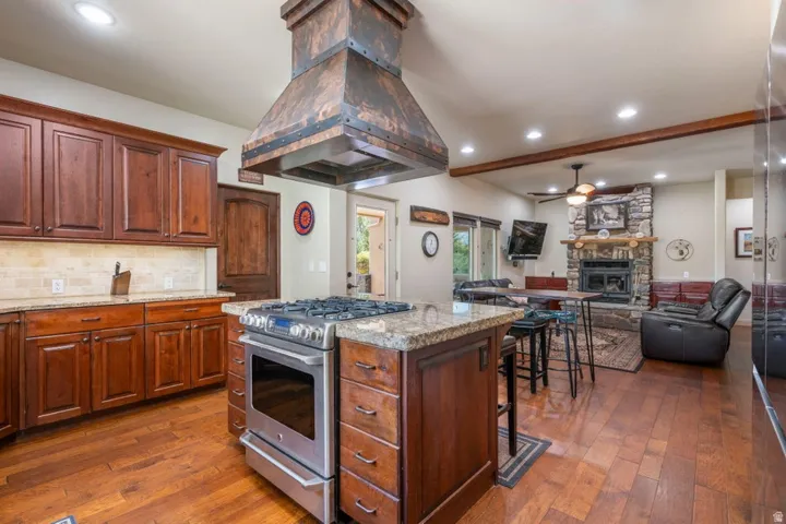 Gourmet kitchen with wood-finish flooring, custom wood cabinetry, and a granite-topped island with a stainless steel range and custom copper hood