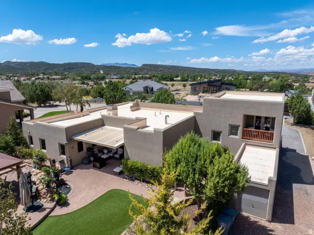Stucco exterior with a balcony featuring a wood railing, a paved patio with a retractable awning, an artificial turf lawn, and a garage with a driveway