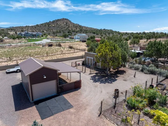 Metal-roofed outbuilding with attached carport, gravel driveway, fenced enclosures, and established garden beds