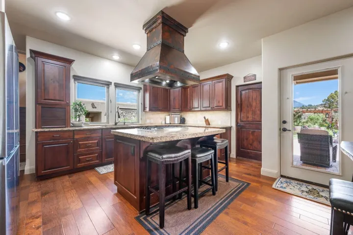 Kitchen featuring rich wood cabinetry, granite countertops, a custom range hood, recessed lighting, and wood-finish flooring