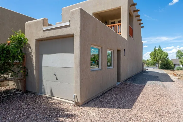Stucco exterior, integrated garage, upper-level balcony with wooden railing, multiple windows, and a gravel driveway