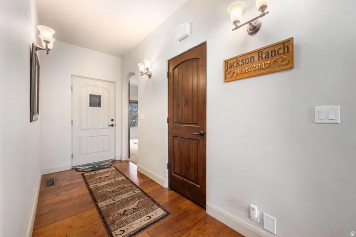 Hardwood flooring, arched doorway, panel doors, and wall-mounted lighting fixtures