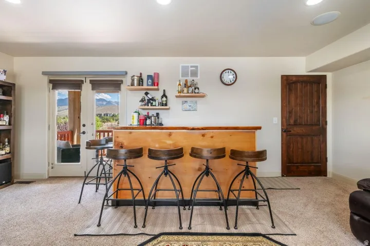 Built-in wet bar with wood countertop, light carpet flooring, recessed lighting, and a dark wood paneled door