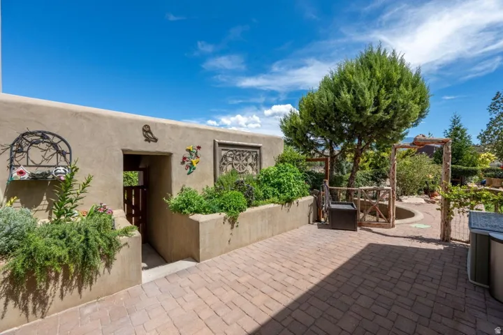 Paved patio area, raised planters with established greenery, exterior wall with architectural detailing, built-in gated entryway, and mature landscaping