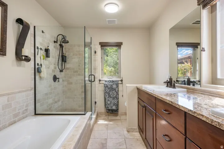 Glass-enclosed shower with subway tile surround, separate soaking tub, wood-finish vanity with stone countertop, and integrated rectangular sink