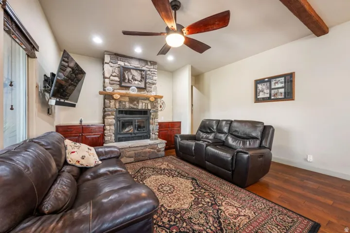 Stone-clad fireplace with a wood mantle, wood-finish flooring, and exposed ceiling beams