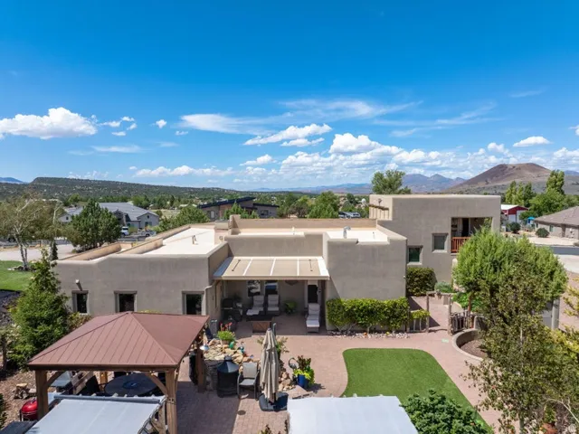 Stucco exterior with a flat roofline, extensive paved patio, covered outdoor living area, built-in planters, and a turf lawn area