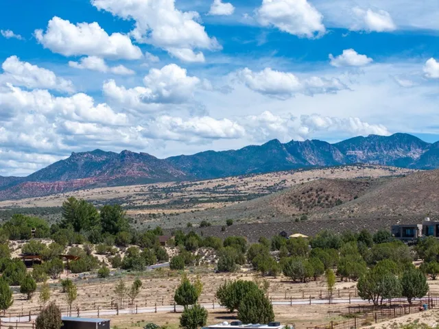 Expansive landscape featuring distant mountains, rolling hills, and scattered vegetation under a blue sky with clouds