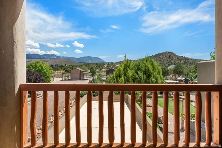 Upper-level balcony with wood railing and stucco wall, offering expansive mountain scenery and a clear sky backdrop
