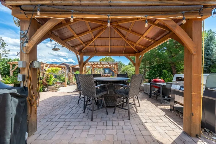 Expansive outdoor living area featuring a wooden gazebo with integrated lighting, a metal roof, and paver stone flooring