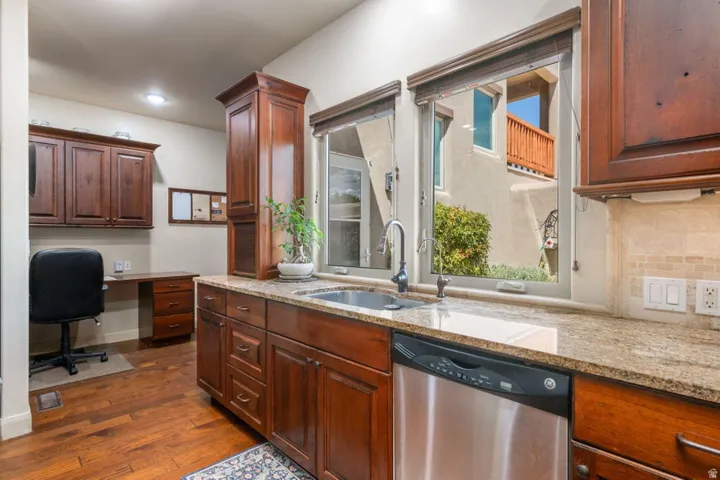 Warm wood-finish flooring, rich wood cabinetry, granite countertops, stainless steel sink, and a stainless steel dishwasher