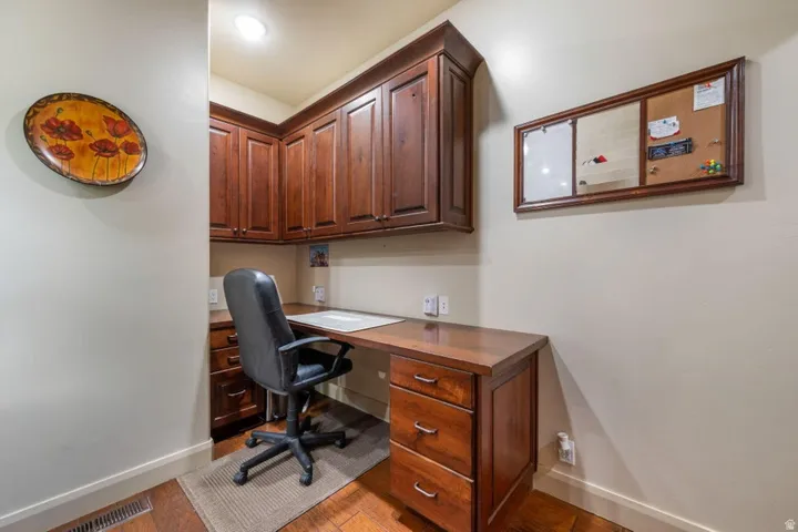 Built-in wood-finish desk with drawer storage, overhead wood-finish cabinetry, recessed ceiling lighting, and wood-finish flooring