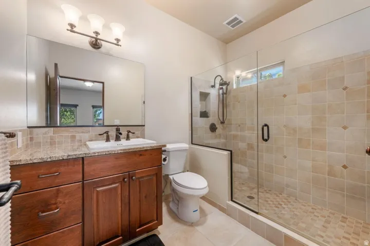 Glass-enclosed shower with tiled walls and floor, vanity with wood-finish cabinetry, countertop, and a vessel sink with dark-toned fixtures