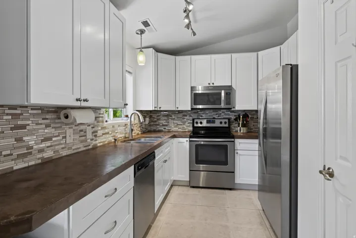 Kitchen with white shaker cabinetry, stainless steel appliances, mosaic tile backsplash, and dark countertops