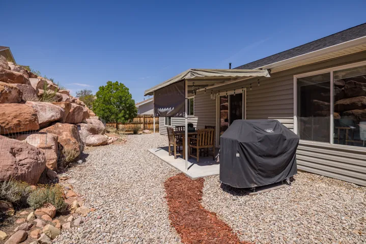 Paved patio with an awning, gravel landscaping, and a substantial rock retaining wall