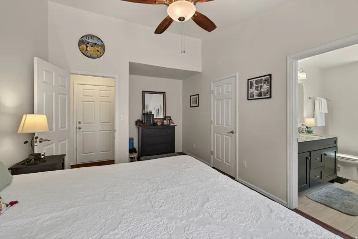 Vaulted ceiling with a wood-finish ceiling fan, panel doors, and a bathroom entry featuring a vanity with a stone-finish countertop