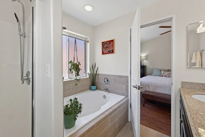 Soaking tub with tiled surround, walk-in shower with glass enclosure, single vanity with light-toned countertop, and recessed lighting