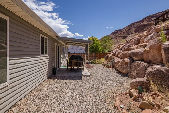 Exterior with horizontal siding, concrete patio, gravel landscaping, and a natural rock retaining wall