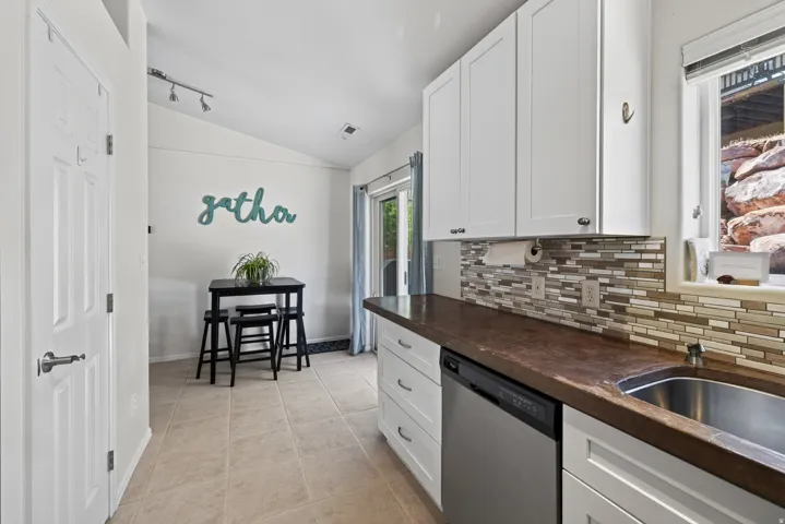 Kitchen featuring white shaker-style cabinetry, a multi-tone tile backsplash, built-in stainless steel dishwasher, and a stainless steel sink