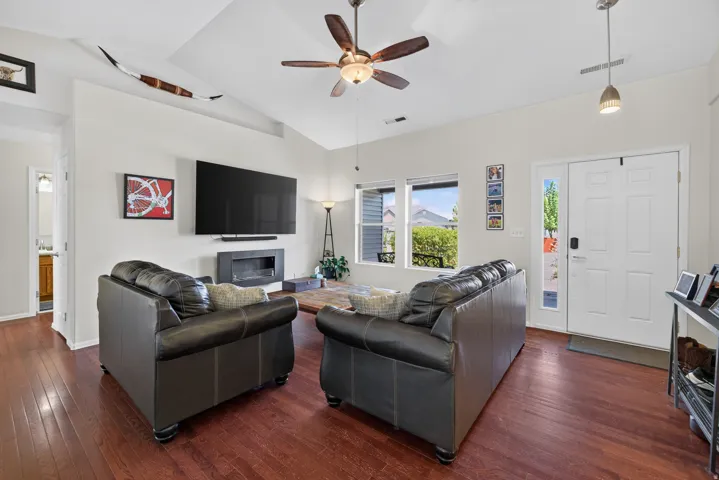 Hardwood flooring throughout, vaulted ceiling, modern fireplace, multiple windows, and a ceiling fan with integrated lighting
