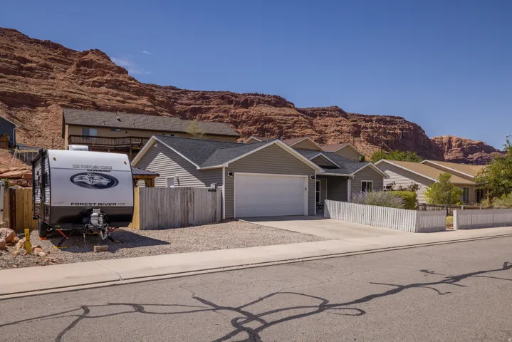 Siding exterior with an attached garage, a gravel parking area, and a white picket fence