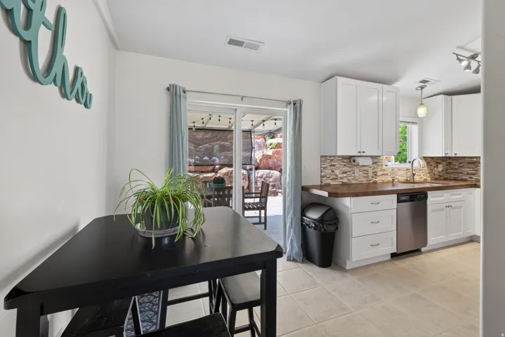 Kitchen featuring white cabinetry, stainless steel dishwasher, tile flooring, and a sliding glass door to an outdoor patio