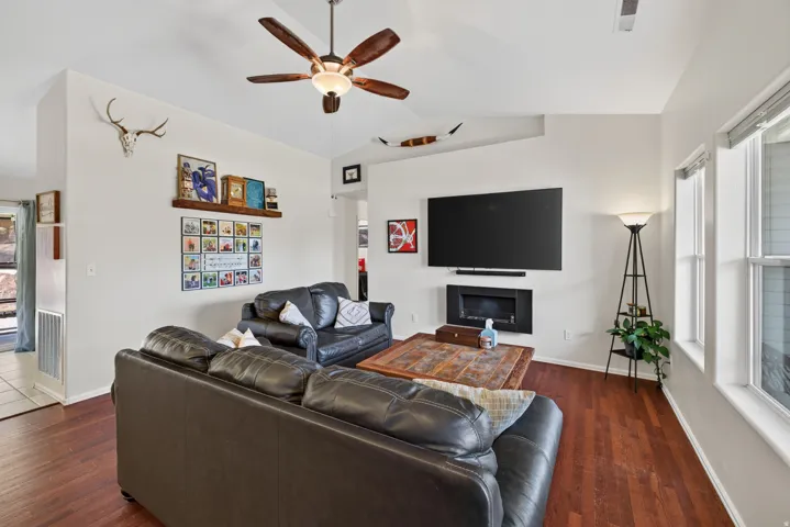 Vaulted ceiling, wood-finish flooring, mounted electric fireplace, recessed wall alcove, and ceiling fan with integrated lighting