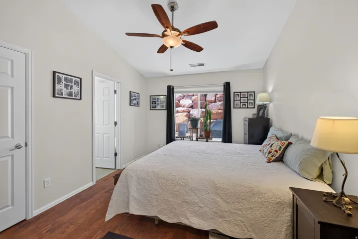 Vaulted ceiling, wood-finish flooring, ceiling fan with integrated lighting, white interior doors, and a window with black curtains