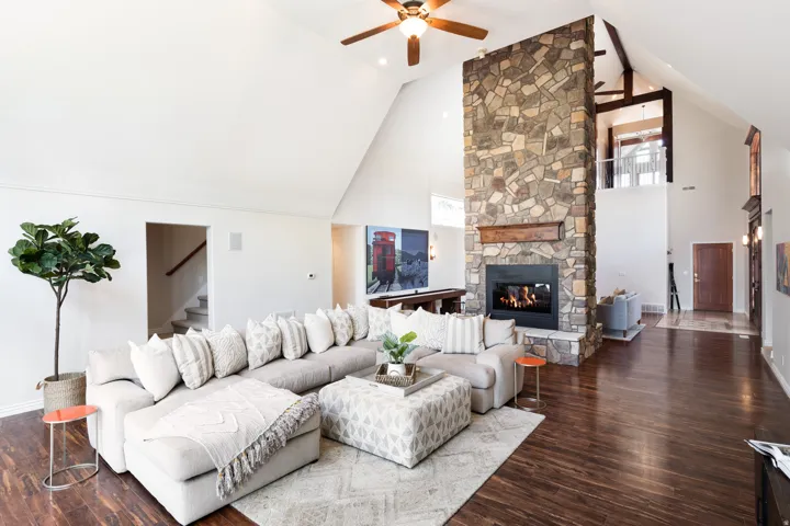 Vaulted ceilings with exposed beams, stone fireplace with a wood mantle, rich wood-finish flooring, and a second-level open railing