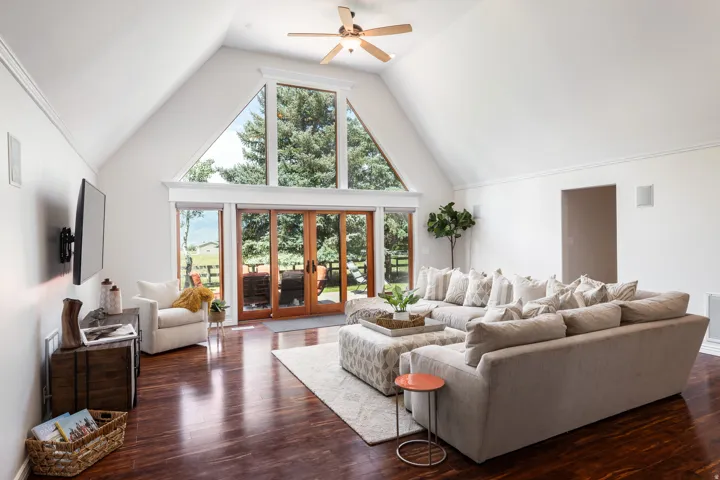 Vaulted ceiling with a ceiling fan, expansive windows, glass-paneled patio doors, rich wood-finish flooring, and integrated wall speakers