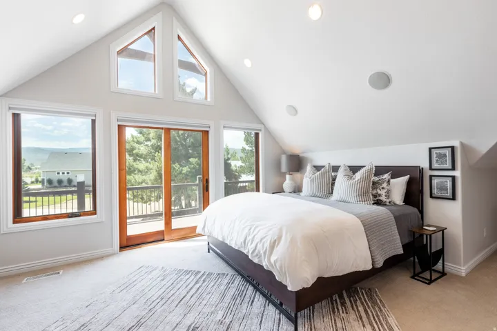 Pitched ceiling with recessed lighting and integrated audio, wood-frame sliding glass doors, multiple large windows, and an exterior balcony with railing