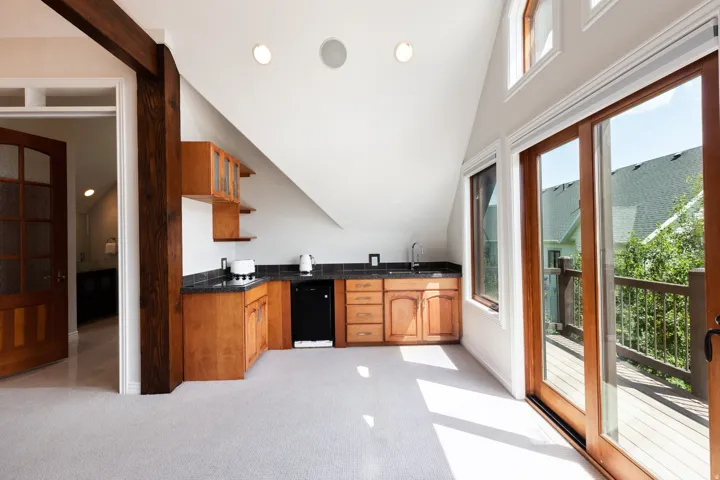 Angled ceiling architecture with recessed lighting, wood-finish cabinetry, dark countertops, and sliding glass door access to a wooden deck