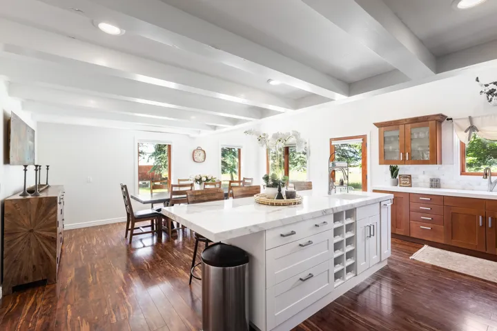Vaulted ceiling with exposed beams, wood-finish flooring, white kitchen island with integrated wine storage, white countertops, and wood cabinetry