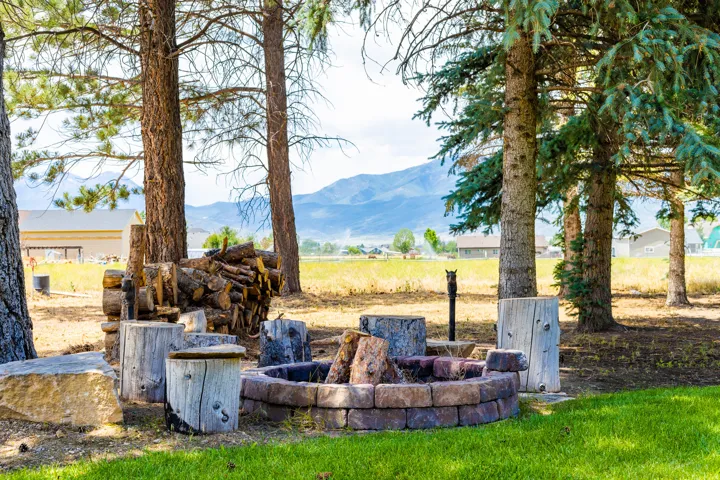 Stone-edged fire pit surrounded by mature trees, featuring a mountain backdrop