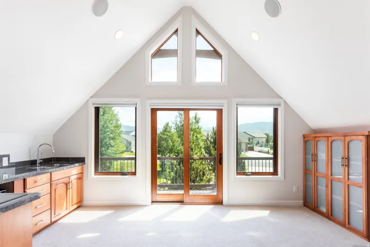 Vaulted ceiling with recessed lighting, integrated speakers, and a wood-finish wet bar with dark countertops