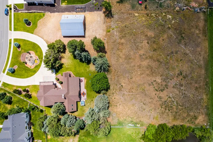 Expansive property featuring a residence with a brown roof, a detached outbuilding with a metal roof, a curved driveway, and a large undeveloped parcel
