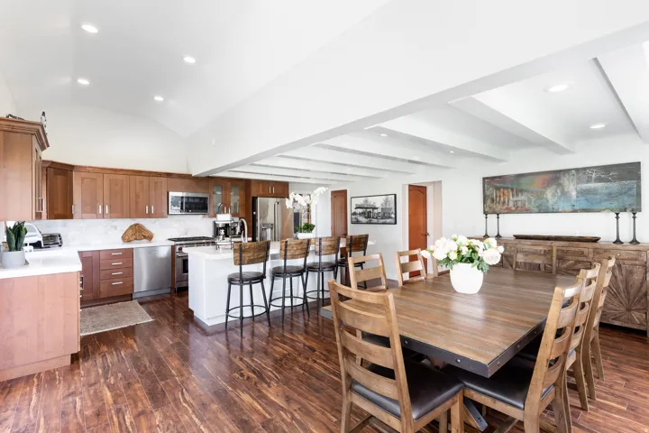 Open-concept kitchen and dining area featuring wood-finish flooring, vaulted ceilings, and a kitchen island with seating