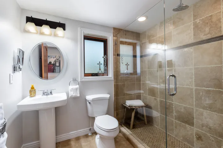 Pedestal sink with chrome fixtures, a round mirror, and a three-light vanity fixture