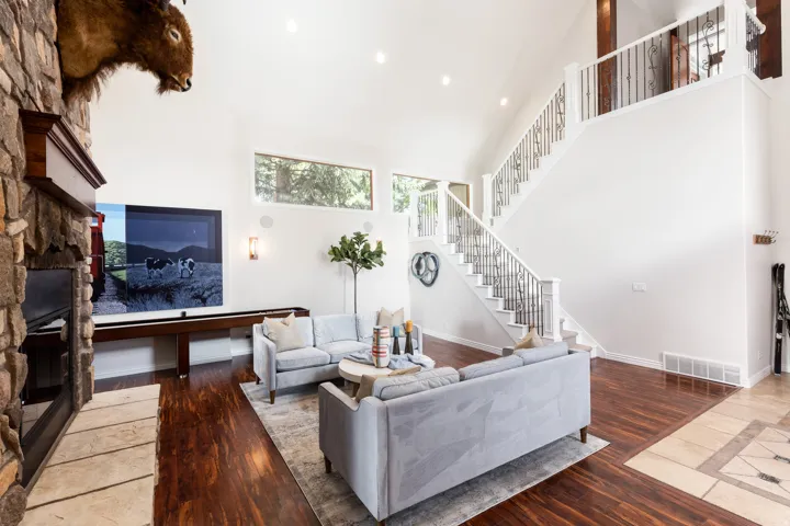 Vaulted ceiling with recessed lighting, stone-clad fireplace with mantel, dark wood-finish flooring, and a staircase featuring decorative metal balusters