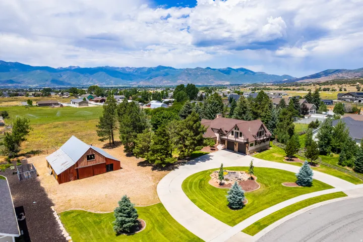 Spacious property featuring a large residence with an attached garage, a separate barn structure, expansive manicured lawns, and a circular paved driveway