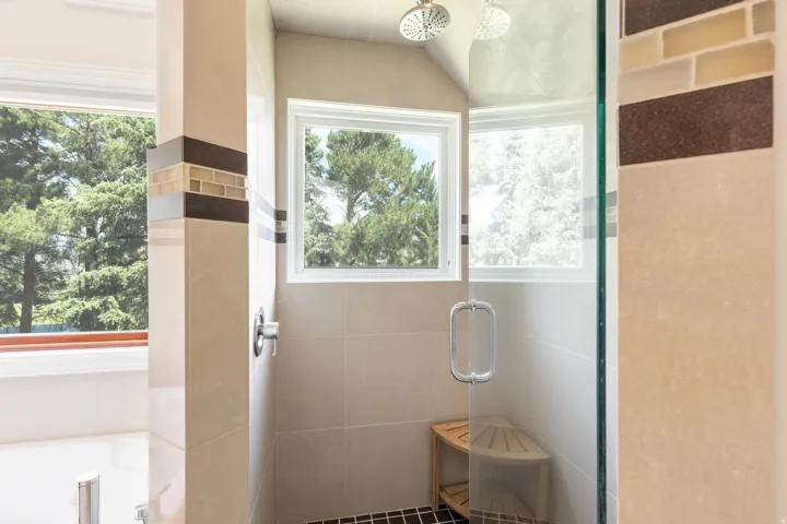 Shower enclosure featuring a glass door, dual shower heads, and tile surround with decorative accent bands